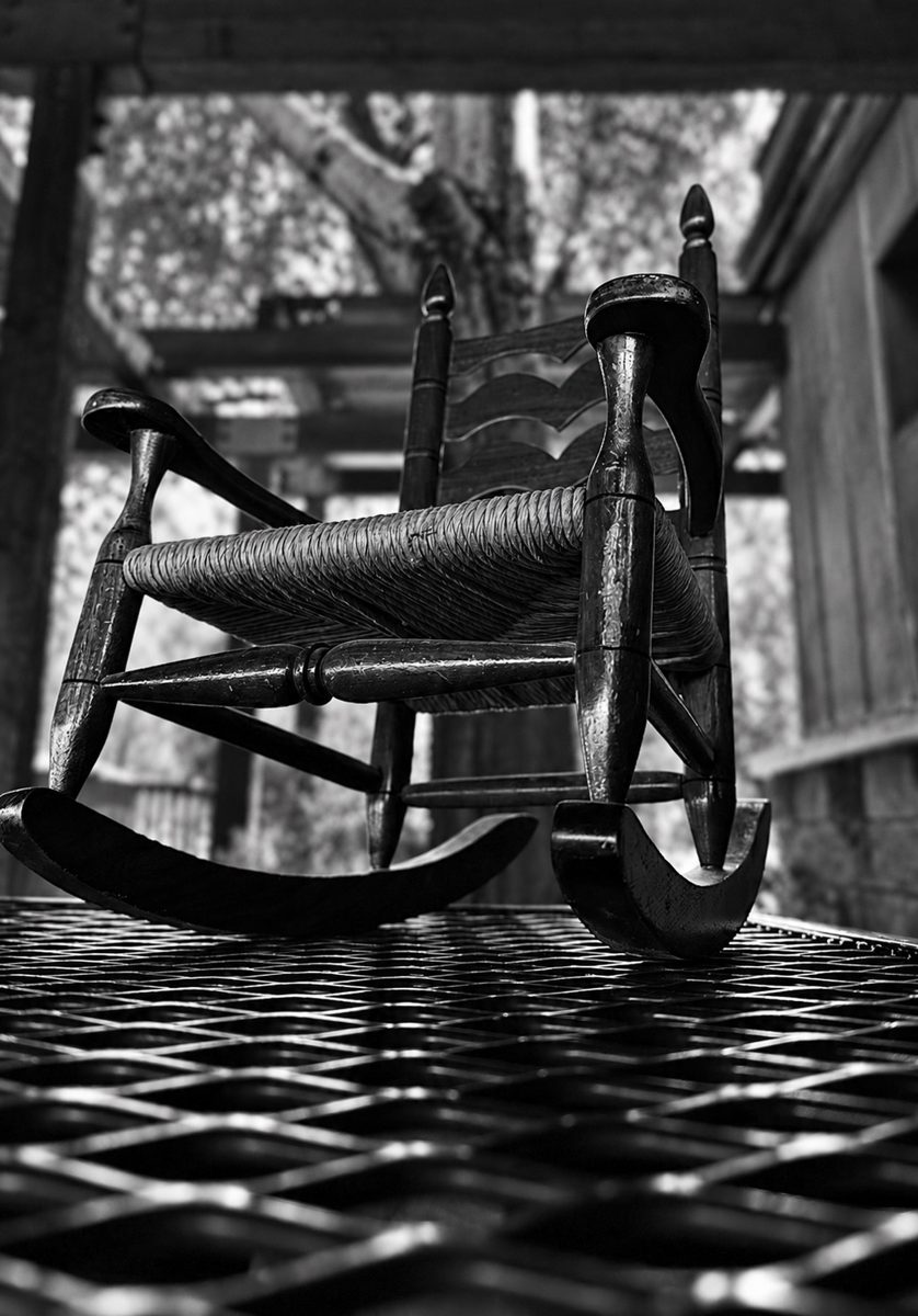 Black-and-white photograph of a porch rocking chair and patterned floor shadows.