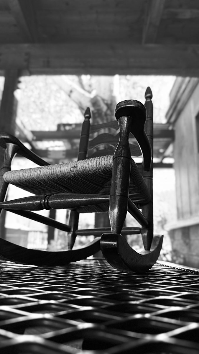 Black-and-white photograph of a porch rocking chair with long shadows.