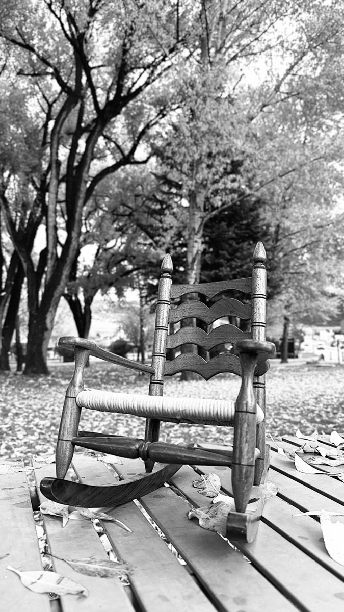 Black-and-white photograph of a rocking chair beside trees.