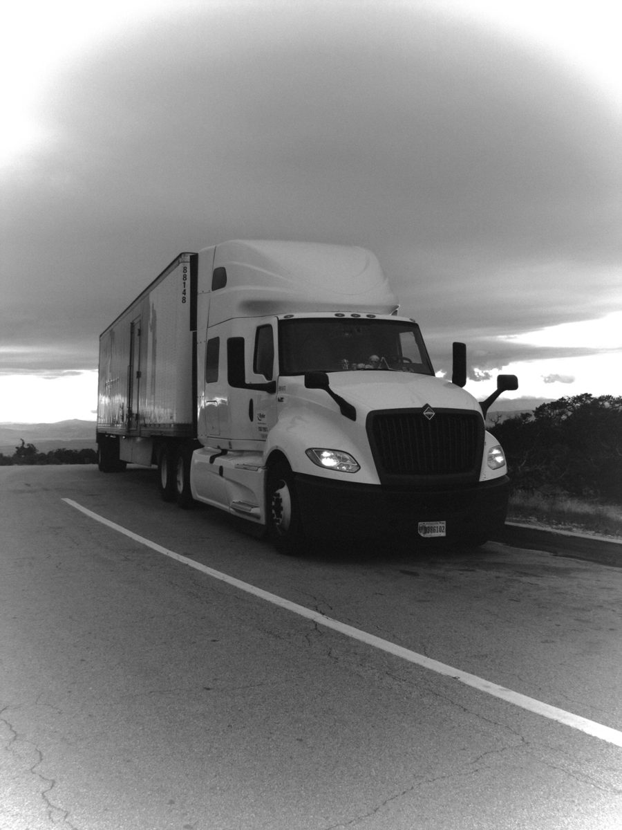 Black-and-white photograph of a semi truck beneath a dramatic cloud.